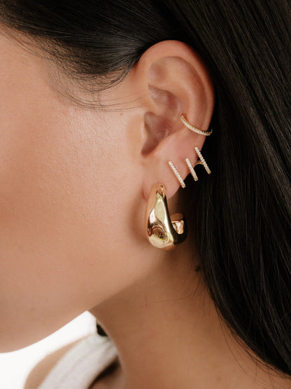 A close-up of a model's ear adorned with multiple gold and diamond earrings, showcasing varied designs. The background is softly blurred, emphasizing the jewelry's detail against smooth skin.