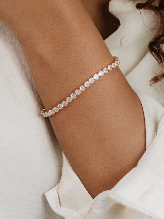 A delicate bracelet adorned with sparkling stones encircles a wrist. The skin tone is warm, and the person is wearing a light-colored, textured shirt.