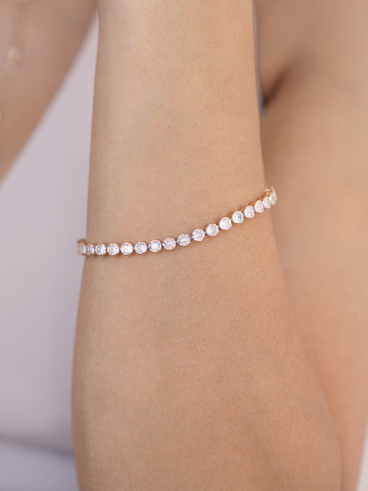 A delicate bracelet adorned with sparkling stones is gracefully positioned on a smooth, tanned forearm. The soft background enhances the elegance of the jewelry against the skin.