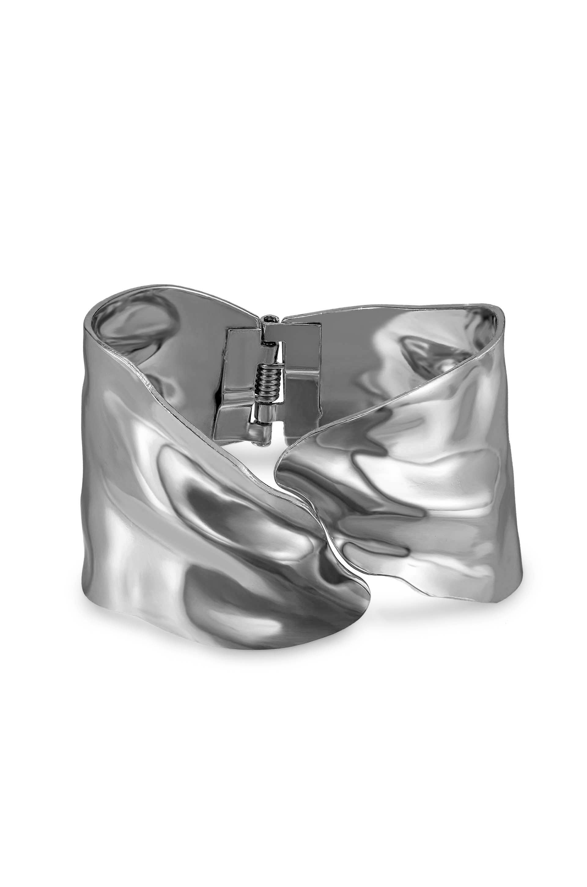 A metallic, wavy cuff bracelet sits open, reflecting light with a polished surface. The clasp is visible at the back, indicating its functionality as a piece of jewelry.