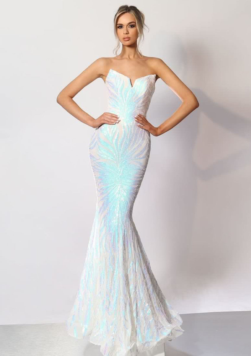 A woman stands confidently in a shimmering, strapless, white evening gown with iridescent detailing. The elegant dress flares at the hem, set against a minimalist backdrop.