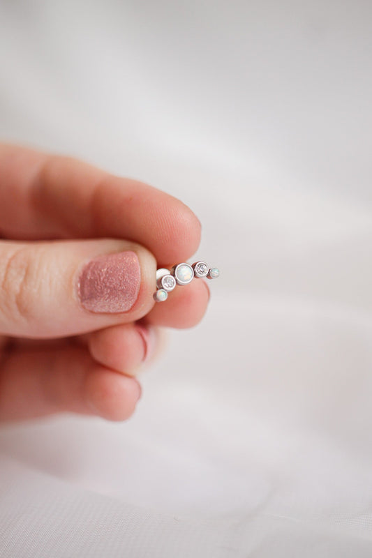 A hand holds a delicate, multi-stone piece of jewelry featuring opals and sparkling gems. It contrasts against a soft, white background, suggesting a display of elegance.