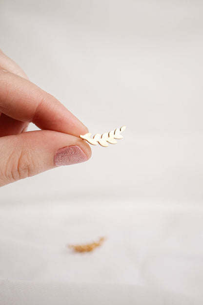 A hand holds a small, intricate leaf-shaped embellishment. It's being examined closely against a soft, muted background, with another similar piece slightly out of focus in the foreground.