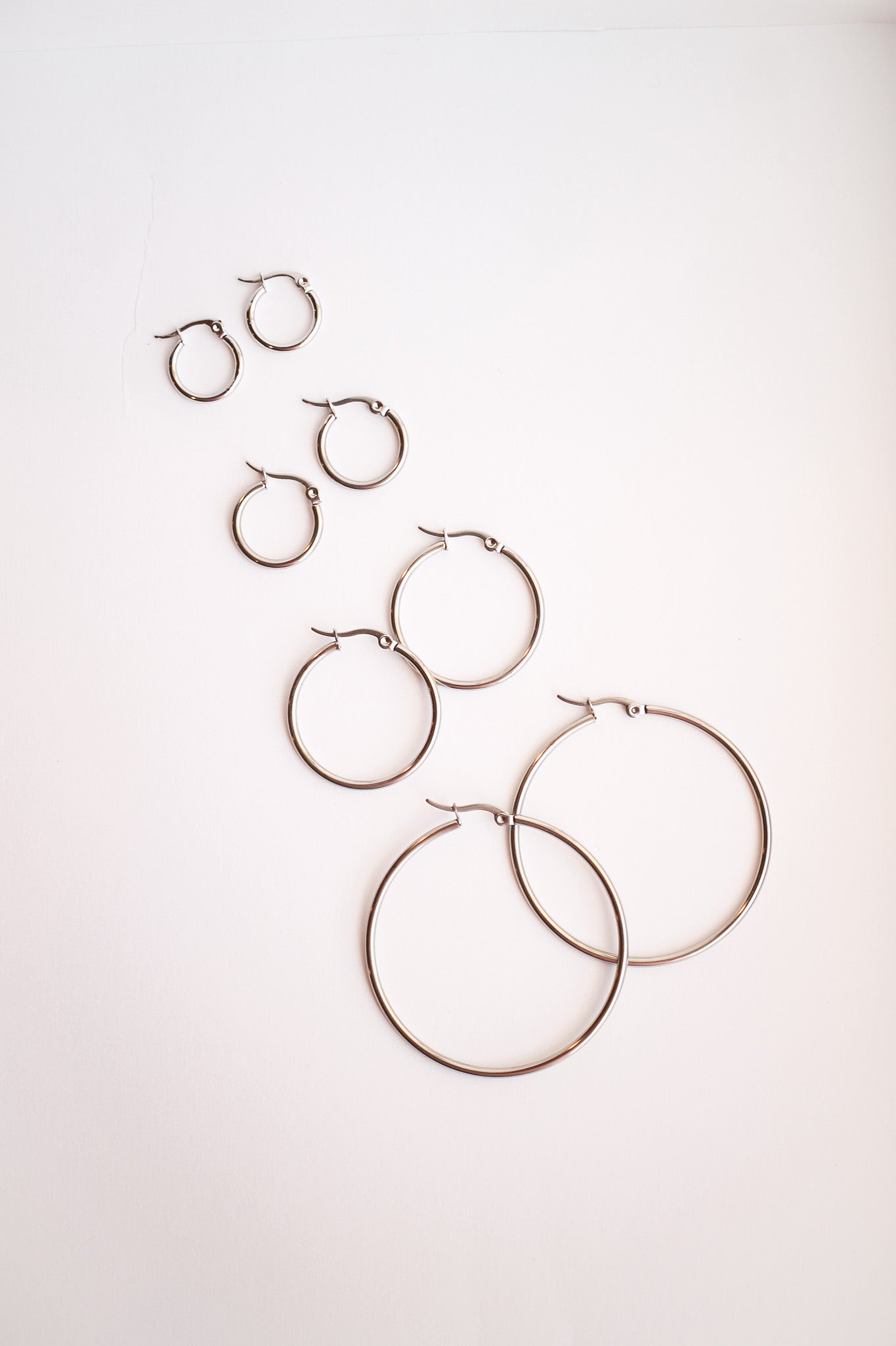 Several pairs of metallic hoop earrings, varying in size, arranged in a diagonal pattern on a pale background, showcasing their shine and design.