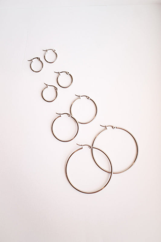 Several pairs of metallic hoop earrings, varying in size, arranged in a diagonal pattern on a pale background, showcasing their shine and design.