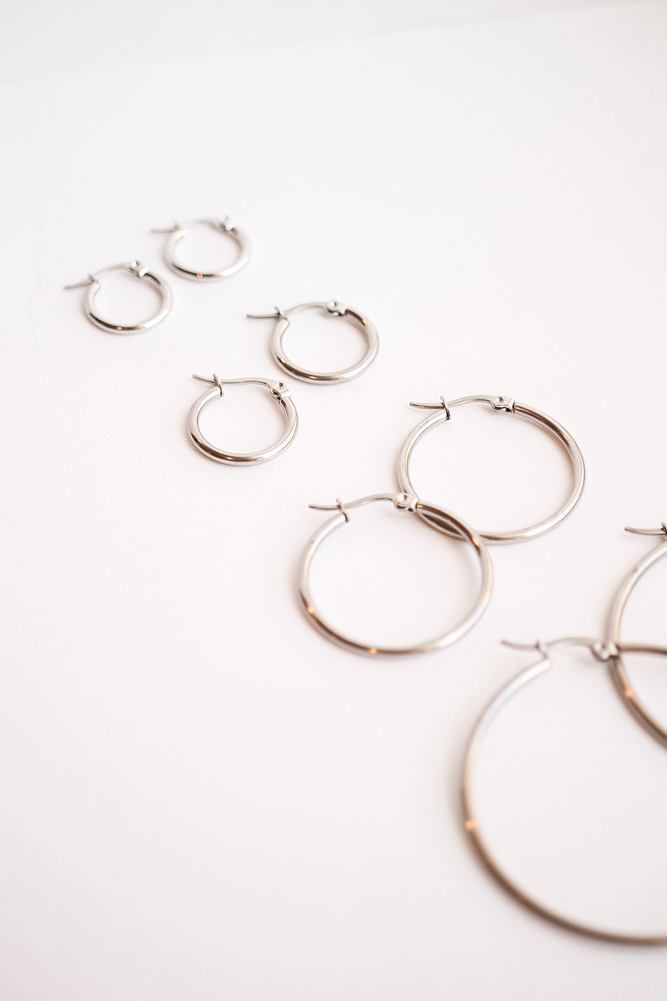 Silver hoop earrings of varying sizes are arranged in a row on a white background, showcasing their reflective surfaces and simple design.