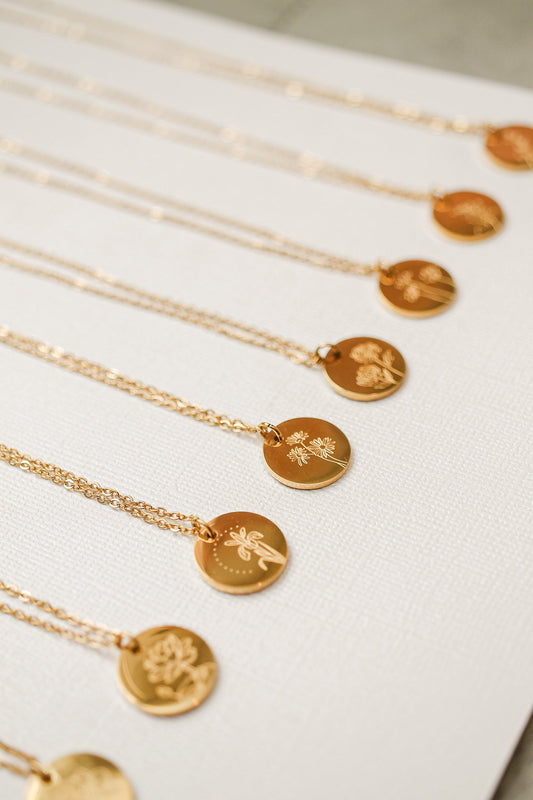 Gold necklaces with circular pendants are displayed side by side. Each pendant features unique floral engravings, resting on a textured light-colored background.