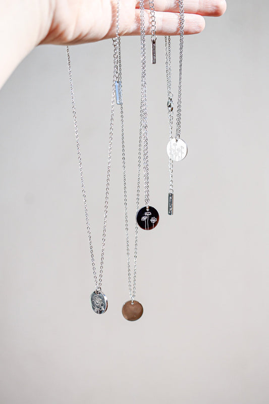 A hand holds several silver necklaces, each displaying different pendants. The background is neutral, enhancing the visual focus on the delicate jewelry.