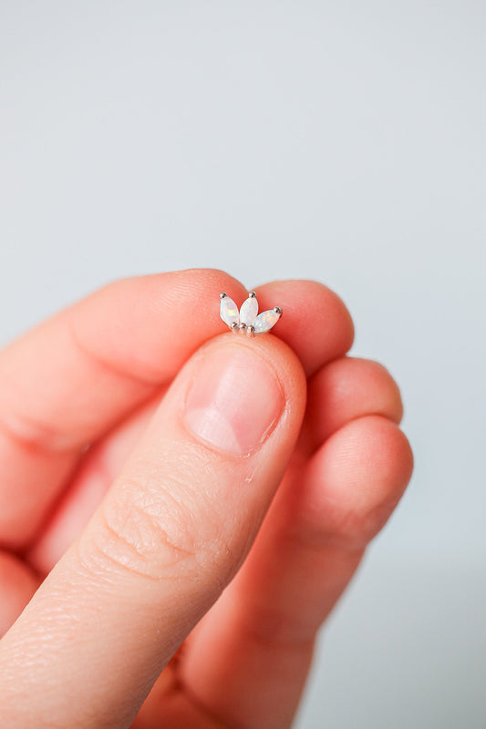 A hand is holding a small, decorative piece resembling a flower with three petal-like elements, showcasing iridescent colors against a soft, neutral background.