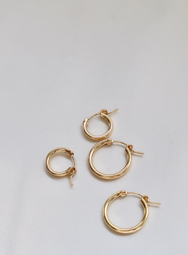 Four pairs of gold hoop earrings of varying sizes are arranged on a soft, light-colored fabric surface, showcasing their circular design and shiny finish.