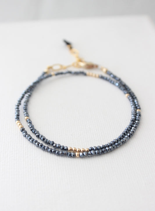 A delicate bracelet made of alternating black and gold beads rests on a light-textured surface, showcasing its intricate design and shimmering elements, suggesting elegance and sophistication.