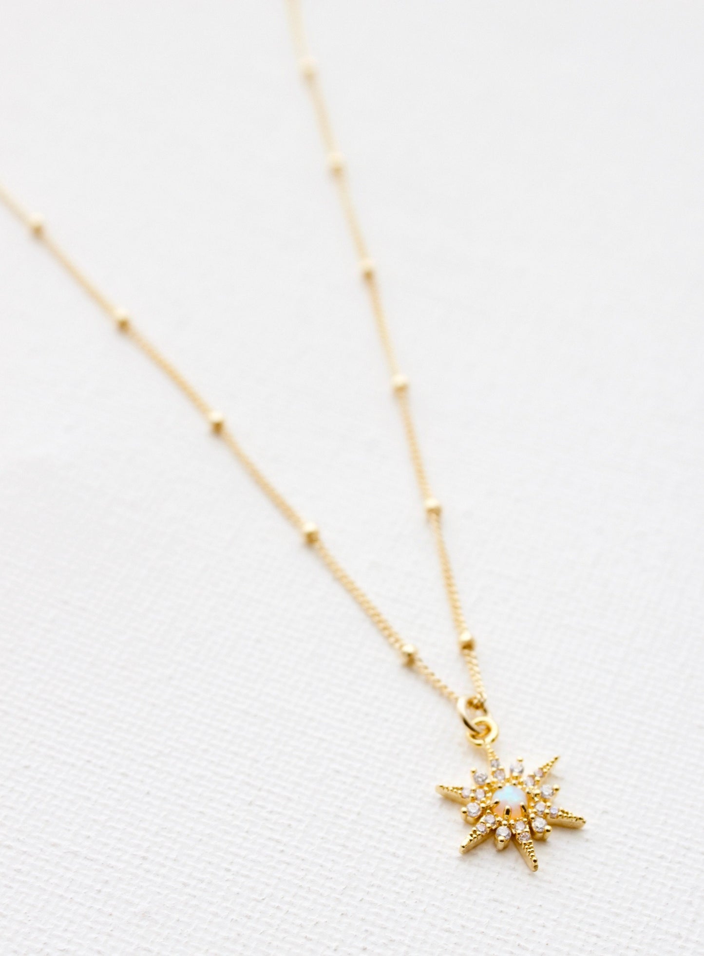 A delicate gold necklace features a star-shaped pendant adorned with small sparkling stones. It rests on a textured white background, highlighting its intricate design and craftsmanship.