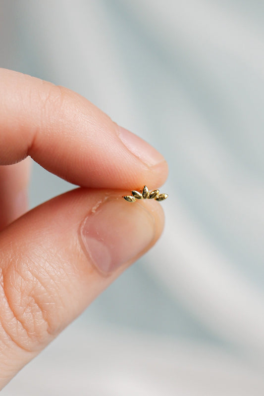 A person holds a small, ornate gold piece with five pointed shapes at the top. The hand's skin appears soft, against a softly blurred light background.