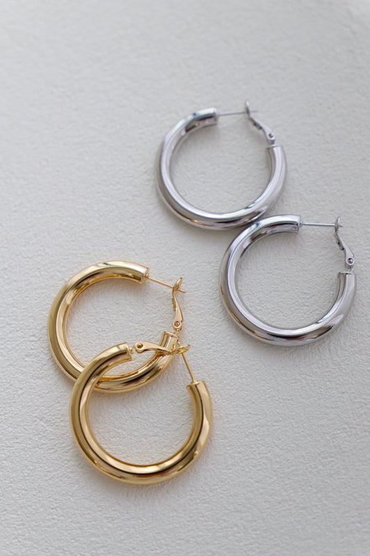 Two pairs of hoop earrings, one gold and one silver, rest on a textured white surface, showcasing their polished surfaces and circular designs, ready for use or display.