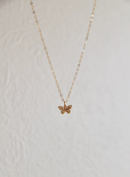 A delicate gold necklace with a small butterfly pendant hangs against a textured, light-colored wall, creating an elegant visual contrast in a serene setting.