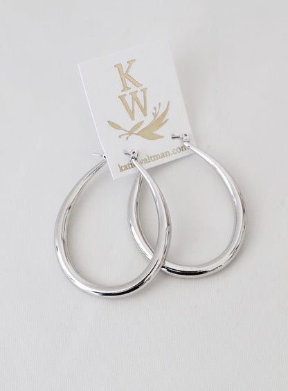 Silver hoop earrings hang from a card displaying "KW" and "kathiwalman.com," placed against a neutral, light-colored surface, emphasizing their polished, sleek design.