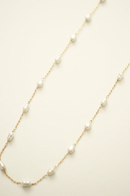 A delicate gold chain features irregularly shaped white pearls spaced along its length, elegantly lying flat against a soft, neutral background.