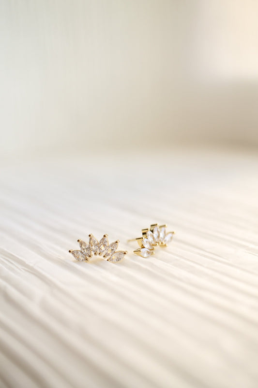 Two pairs of gold earrings, adorned with clear, marquise-cut stones, rest on a softly textured, light-colored surface, showcasing their elegant design in a bright, minimalist setting.