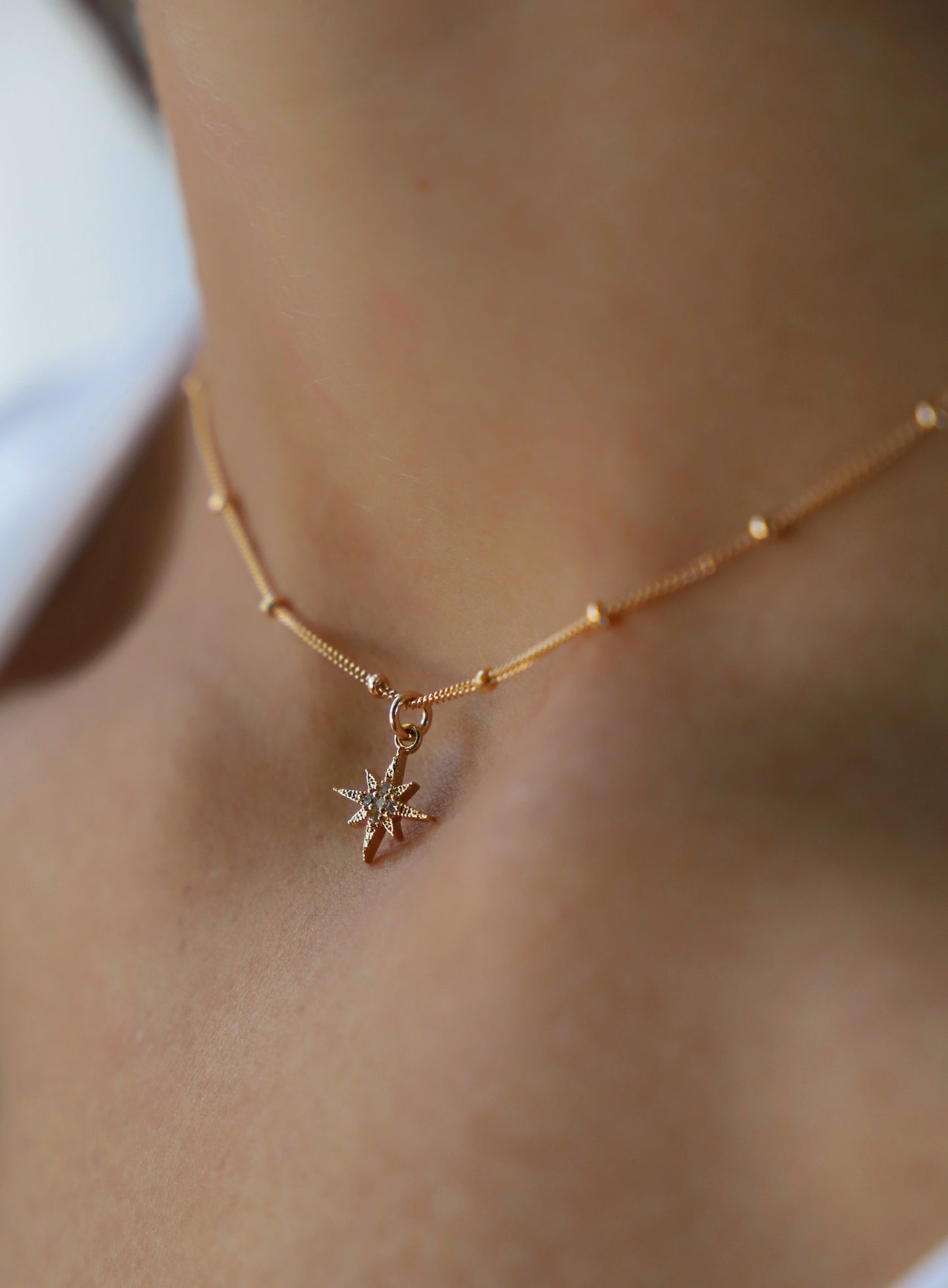 A delicate gold necklace adorned with a star-shaped pendant rests on a woman's neck, highlighting the skin's smooth texture and the soft lighting of the environment.