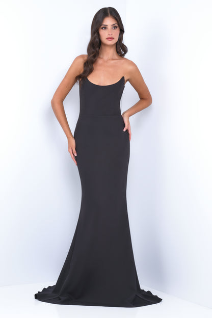 A woman stands confidently, wearing a sleek, black, strapless evening gown. She poses against a light-colored wall, showcasing the dress's elegant silhouette and a minimalist aesthetic.