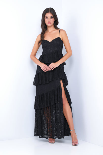 A model stands confidently wearing a black layered lace dress with a thigh-high slit. She has long hair, and the backdrop is a clean, white setting, enhancing the outfit's elegance.