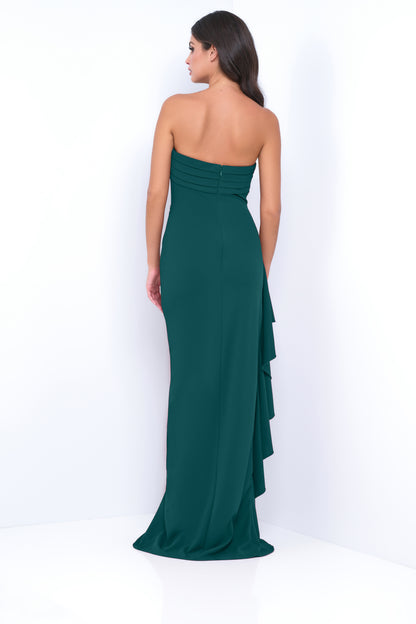 A woman wears a form-fitting, strapless dark teal gown with a cascading ruffle detail at the back, standing against a plain white backdrop, showcasing elegance and sophistication.