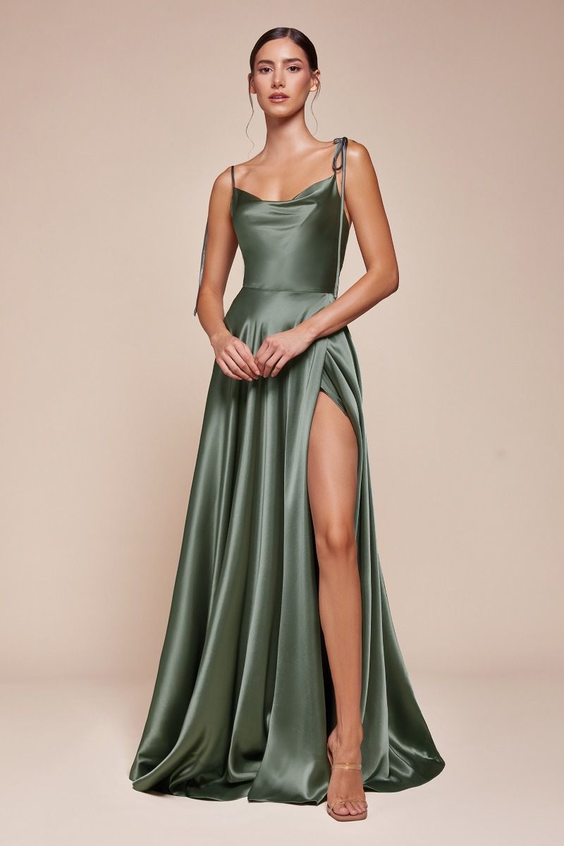 A woman stands confidently in a flowing green satin dress with a high slit, showcasing her leg. The backdrop is a soft beige, enhancing the elegance of the outfit.