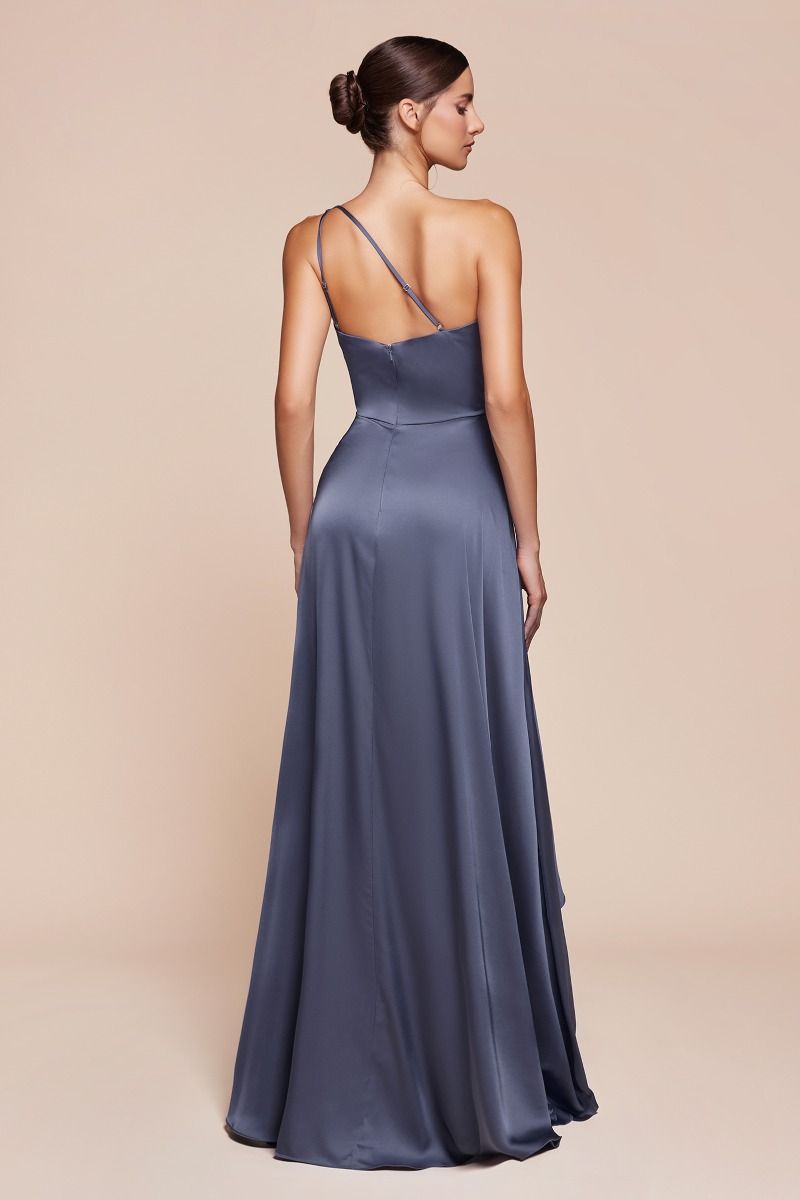 A woman stands gracefully with her back turned, wearing a long, flowing gray satin dress. The backdrop is a smooth, neutral-colored surface, emphasizing her elegant silhouette.