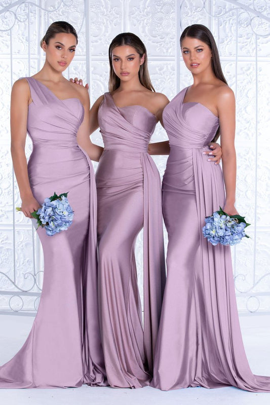 Three women pose together, each wearing elegant, form-fitting lavender gowns. They hold bouquets of blue flowers, standing against a decorative white backdrop, creating a stylish and formal context.