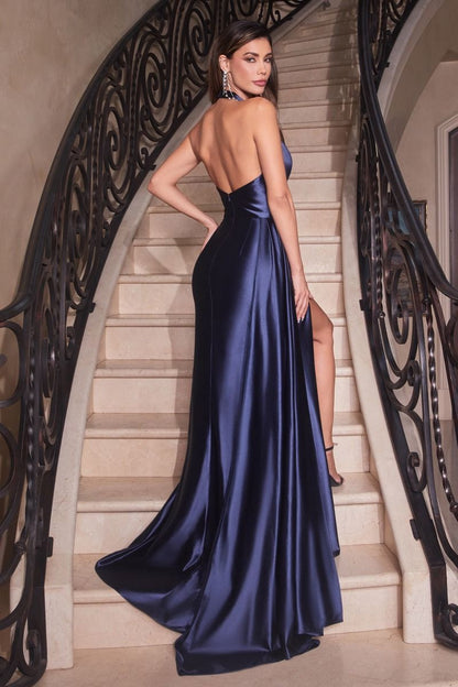 A woman in a long, navy satin gown poses on a staircase, showcasing the dress's elegant slits and backless design, framed by a stylish wrought-iron railing.