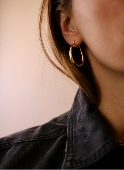 A gold hoop earring adorns a person's ear, while soft brown hair partially frames their face. The background is a gentle beige tone, creating a warm atmosphere.