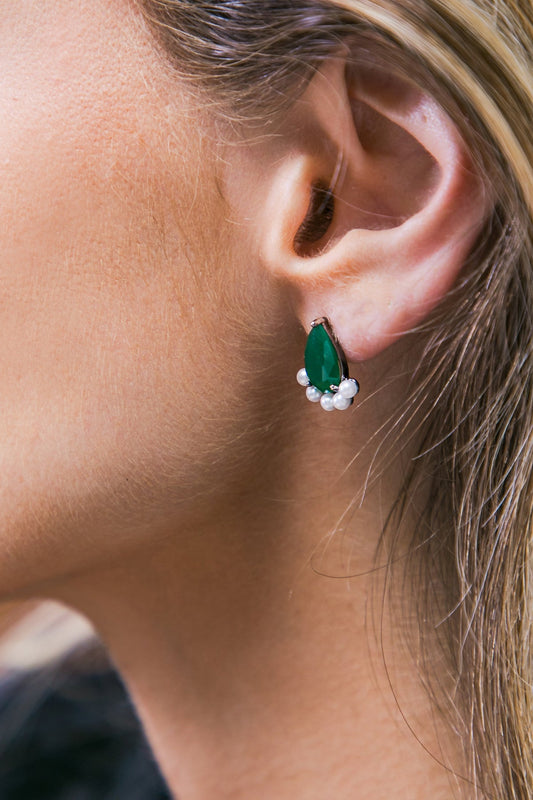 A close-up of a woman's ear features an elegant green teardrop earring adorned with small white pearls, highlighting the ear's curves against smooth skin and flowing hair.