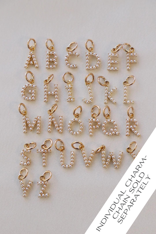 Gold letter charms, embellished with small pearls, are arranged in rows on a light fabric background. Each charm is attached with a small loop for easy attachment. Text: "INDIVIDUAL CHARM-CHAIN SOLD SEPARATELY."