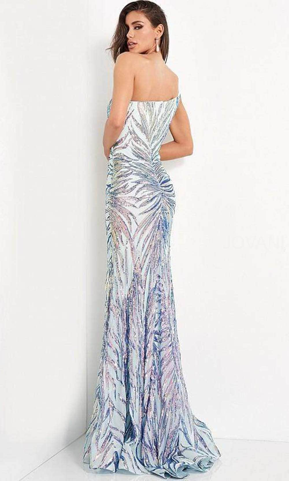 A woman stands against a white wall wearing a glistening, strapless evening gown with a shimmering, feather-like pattern. She gazes back, exuding elegance and confidence.